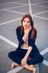 Fototapeta premium Red-haired model in a suit sits in a parking lot in summer