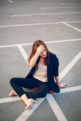 Red-haired model in a suit sits in a parking lot in summer