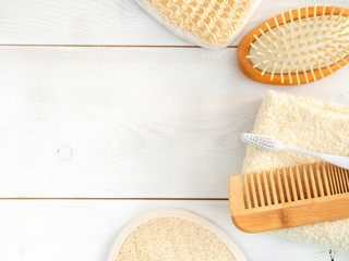 Hygienic bathroom and spa accessories flatlay on wooden table. Wooden hair brush, tooth brush, towel and loofah. Body, face and hair care at home.