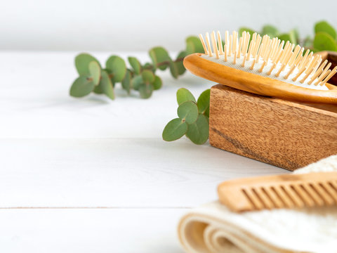 Hygienic bathroom and spa accessories on wooden table. Wooden hair brush and comb, towel and green leaves. Hair care at home.