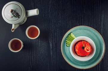 Top view of black table with japanese food salmon tartare on a rustic green dish and two cups of tea