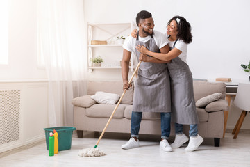 Happy black couple doing household chores together, mopping floor and hugging