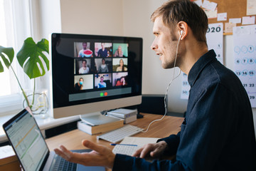 Young man having Zoom video call via a computer in the home office. Stay at home and work from home concept during. Man making notes during virtual video chat conference call telecommute