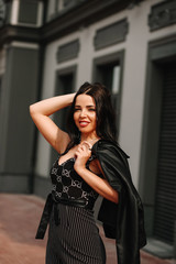 
Beautiful brunette in black overalls, suit, posing on a city street, against the background of a new modern building in dark colors