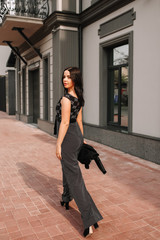 Obraz premium Beautiful brunette in black overalls, suit, posing on a city street, against the background of a new modern building in dark colors