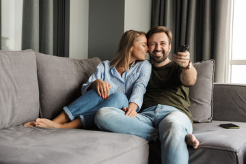 Obraz premium Photo of joyful couple watching TV and using remote control