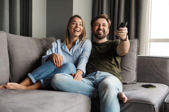 Photo of joyful couple watching TV and using remote control