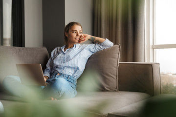 Image of woman using laptop and looking aside while sitting on sofa