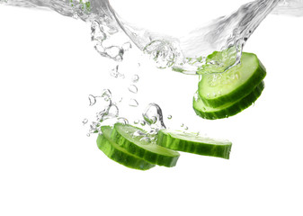 Falling of fresh cucumber slices into water against white background