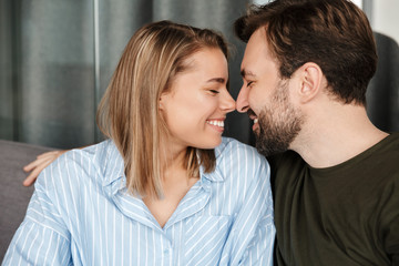 Photo of cheerful couple laughing and hugging while sitting on sofa
