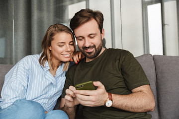 Photo of cheerful beautiful couple smiling and using mobile phone