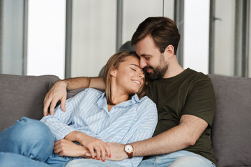 Photo of cheerful couple smiling and hugging while sitting on sofa