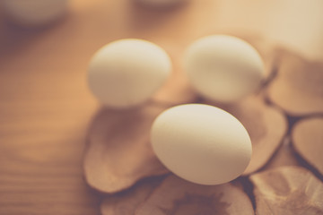 Three white chicken eggs on a wooden board and brown table.