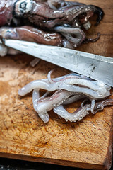 Squid and tentacles on cutting board with knife.