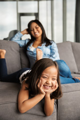 Photo of woman with her daughter laughing while resting on couch