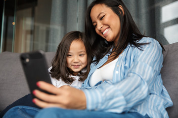 Photo of pregnant woman with her daughter smiling and using cellphone