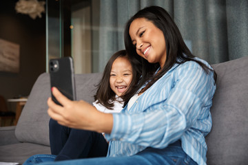 Photo of pregnant woman with her daughter smiling and using cellphone