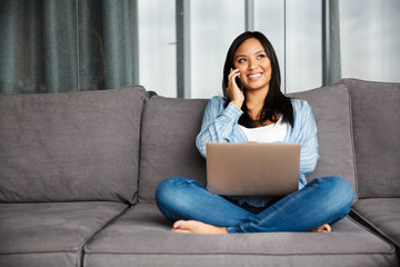 Photo of smiling pregnant woman talking on cellphone and using laptop