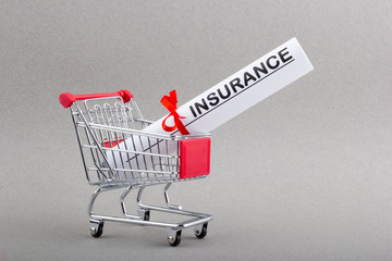 Paper bundle with word insurance and red ribbon in shopping trolley.