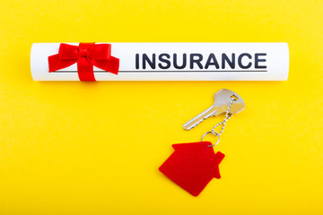 House key with trinket on yellow background and paper bundle with word insurance and red ribbon. Нome insurance concept.