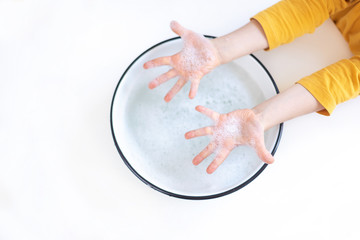Child's hands in foam. The child washes his hands in a container of water