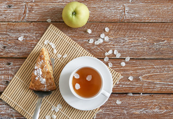 Homemade apple pie with cinnamon and cup of tea on wooden table.