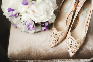 Brides wedding shoes with a bouquet with roses and other flowers on tha arm chair