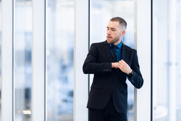 Portrait of handsome man standing in a suit and tie in front of glass door