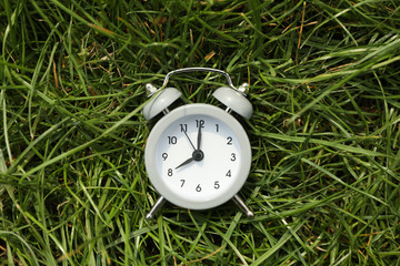 Alarm clock on green grass background. Springtime