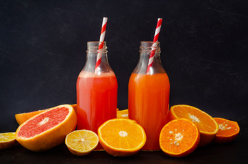 orange, grapefruit juice in glass bottles on a dark concrete background with fruits