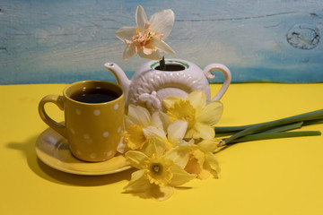 Next to a cup of tea is a bouquet of daffodils. There is one white daffodil in the teapot.