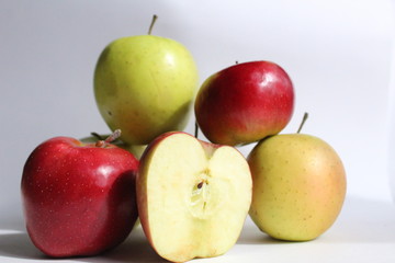 three or more red yellow green apples are stacked together on a white light gray background