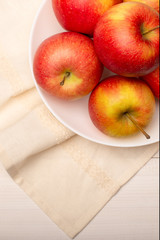 Top view of ripe red apples in a bowl on white wooden table, close up, vertical view