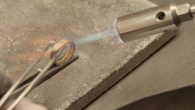 jeweler soldering pieces of gold on top of golden ring