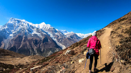 Fototapeta premium A woman trekking on the Annapurna Circuit Trek, Himalayas, Nepal. Panoramic view on snow caped Annapurna chain. Lots of dried grass. High altitude, massive mountains. Freedom and adventure