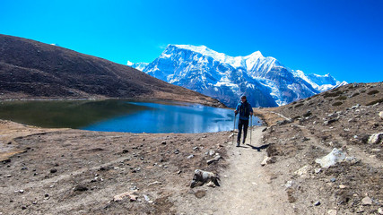 Naklejka premium A man trekking along the Ice Lake, Annapurna Circuit Trek detour, Himalayas, Nepal, surrounded by high, snow caped mountains. Annapurna Chain in the back. High altitude lake. Harsh landscape.