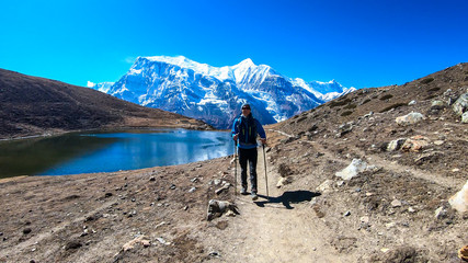 Fototapeta premium A man trekking along the Ice Lake, Annapurna Circuit Trek detour, Himalayas, Nepal, surrounded by high, snow caped mountains. Annapurna Chain in the back. High altitude lake. Harsh landscape.