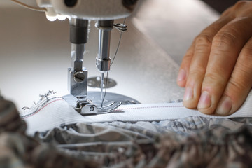 Hand of seamstress is using the white industrial sewing machine to sew elastic strips of pants close-up.