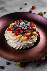 Meringue Pavlova dessert with fresh strawberries and blueberries on a blue plate