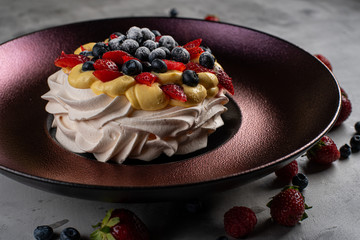 Meringue Pavlova dessert with fresh strawberries and blueberries on a blue plate