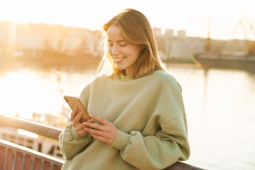 Portrait of happy woman using cellphone while bending over railing