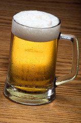 A mug of cold beer over a wooden tabletop.