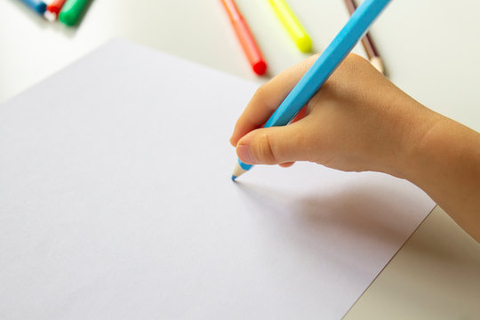 Close up of child's hands drawing at blank white paper with a blue pencil