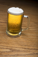 A mug of cold beer over a wooden tabletop.