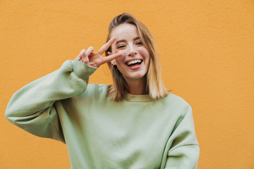Portrait of cheerful blonde woman smiling and gesturing peace sign