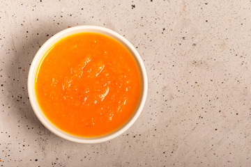 Pumpkin and carrot soup with fresh dill on concrete light background