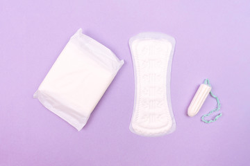 Women's pads and tampon on a purple background, top view.
