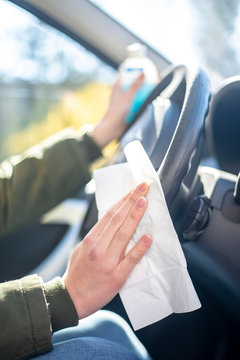 Close-up of woman in car disinfecting steering wheel