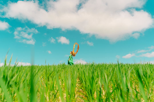 Young woman wearing a green dress standing in a field with blowing ribbons