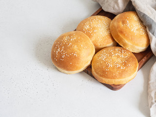 Group crisp fresh homemade buns with sesame on wood tray under a linen towel on a table.